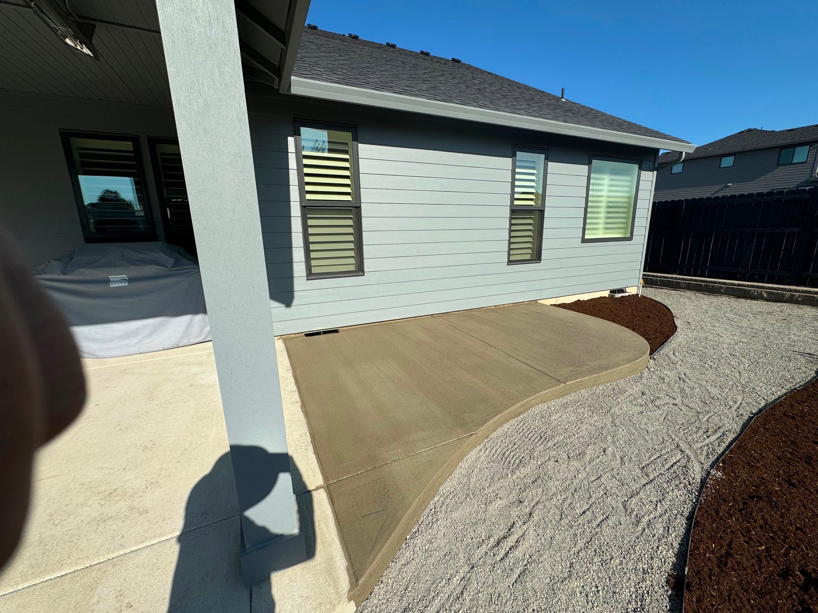 Finished broom-finish concrete patio with a curved edge, bordered by fresh bark mulch and gravel