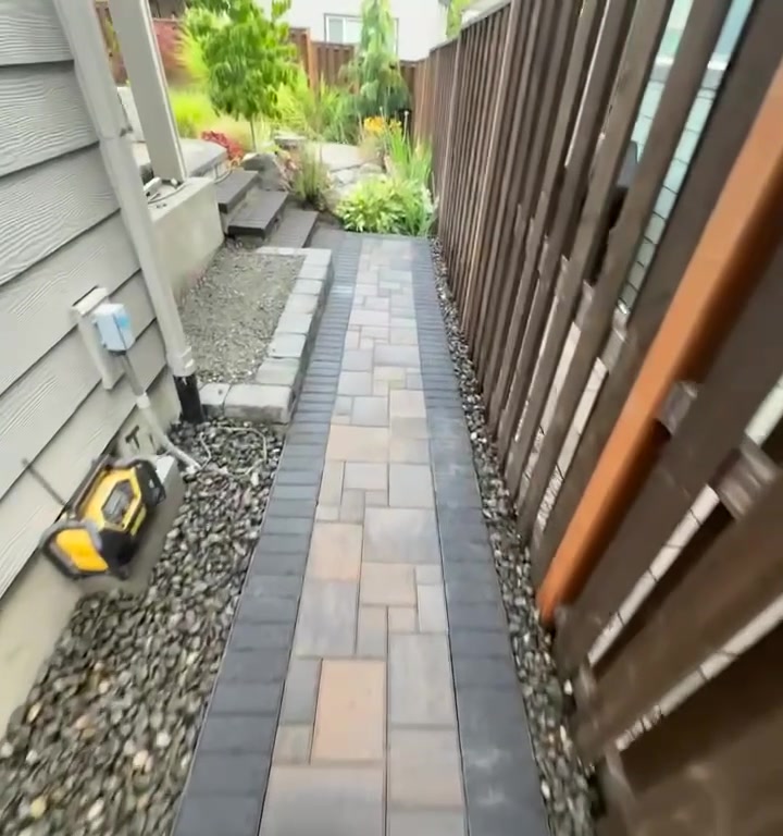 Finished paver side path with river rock drainage borders running between the house and cedar fence